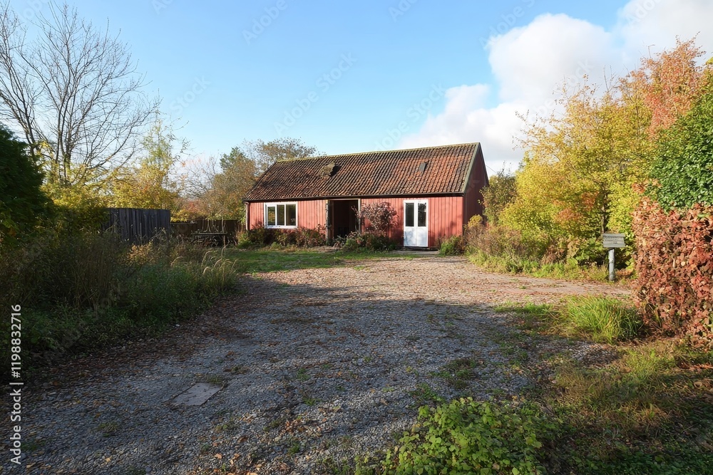 This image showcases an abandoned red building in a serene, overgrown setting. Nature reclaims the space, providing a tranquil atmosphere.