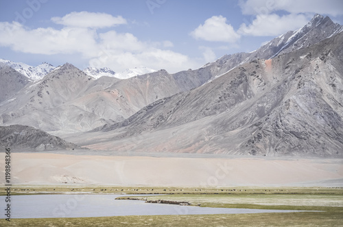 The high-mountain river Murghab flows and meanders among green meadows and fields in a mountain gorge against the background of mountain ranges with rocks and glaciers, near the city of Murgab photo