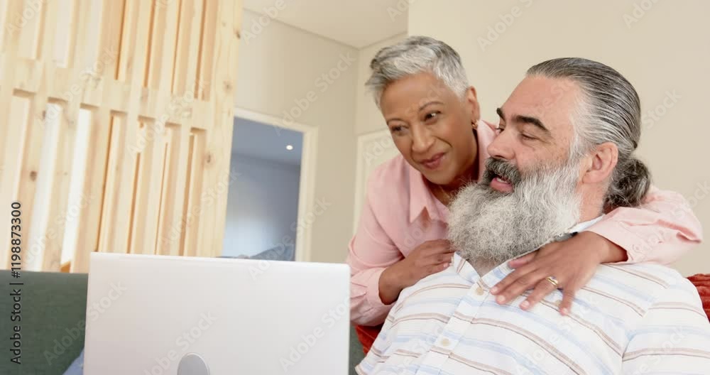 Smiling senior couple using laptop together at home, enjoying online content