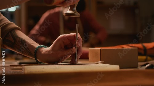 Cropped shot of unrecognizable skillful tanner with tattooed arm using punch tool making leather bag detail working in studio in small scale traditional handmade industry