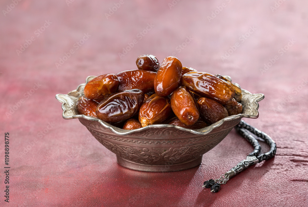 Bowl full of dates and tasbih (misbaha) on old red-brown wooden table.