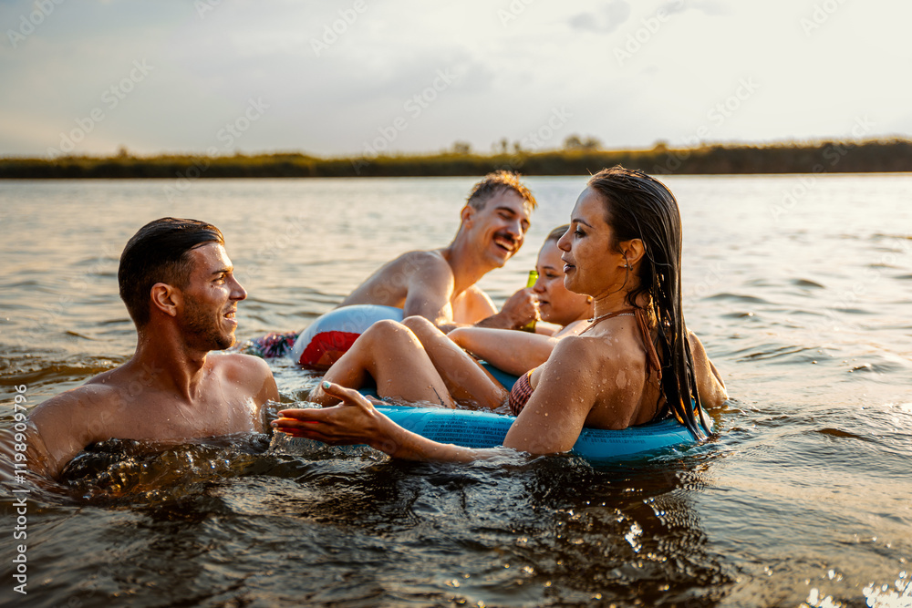 Obraz premium Group of young friends having fun and enjoying a summer day swimming with rubber tube and drinking beer at the lake.