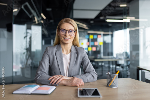 Online business meeting  conference. Mature woman smiling and looking at camera  working inside office with documents and papers. Businesswoman in business suit. Web camera view.