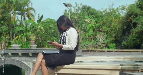 A lady in formal attire using her phone in an outdoor office near a swimming pool. photo