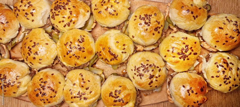 Top-down view of sliders filled with pulled pork, arranged side by side, with buns sprinkled with flax seeds Top-down view of sliders filled with pulled pork, arranged side by side, with buns sprinkled with flax seeds