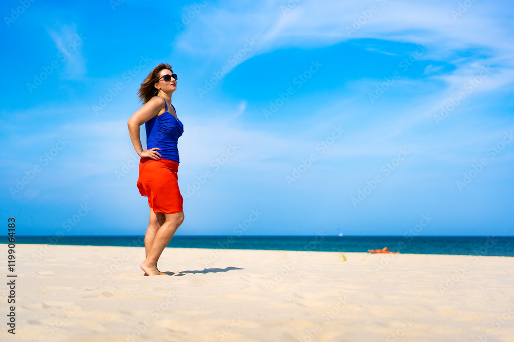 Beautiful middle-aged woman standing and sunbathing on sandy beach. Model in beautiful pose on beach Beautiful middle-aged woman standing and sunbathing on sandy beach. Model in beautiful pose on beach