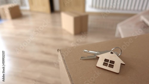 Family with a child moves into a new apartment. Cardboard boxes on the floor. Closeup of apartment keys with house symbol in the foreground. Slow motion video
