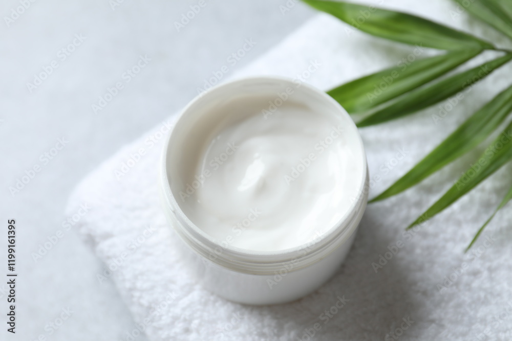 A jar of cream and a palm leaf on a white towel, top view. Professional and beauty products A jar of cream and a palm leaf on a white towel, top view. Professional and beauty products
