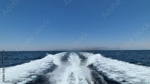 Sea water ship trail with white foamy wave. Speedboat rush. Green forested land of seen. Blue clear sky and good weather.