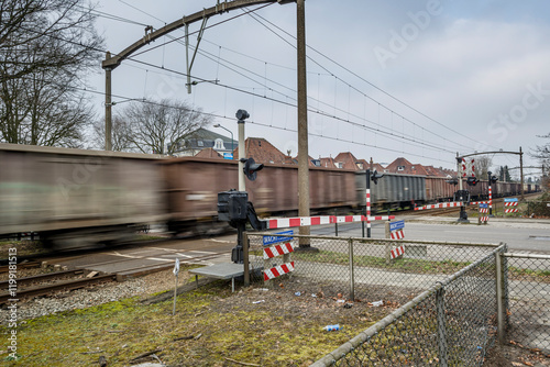 Canvas-taulu Train passes through a level crossing in a residential area with cloudy skies in