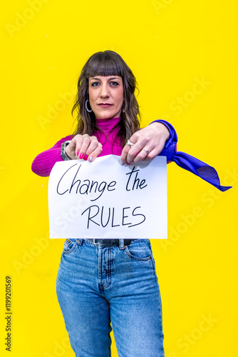 Woman showing a sign that says change the rules on yellow background photo