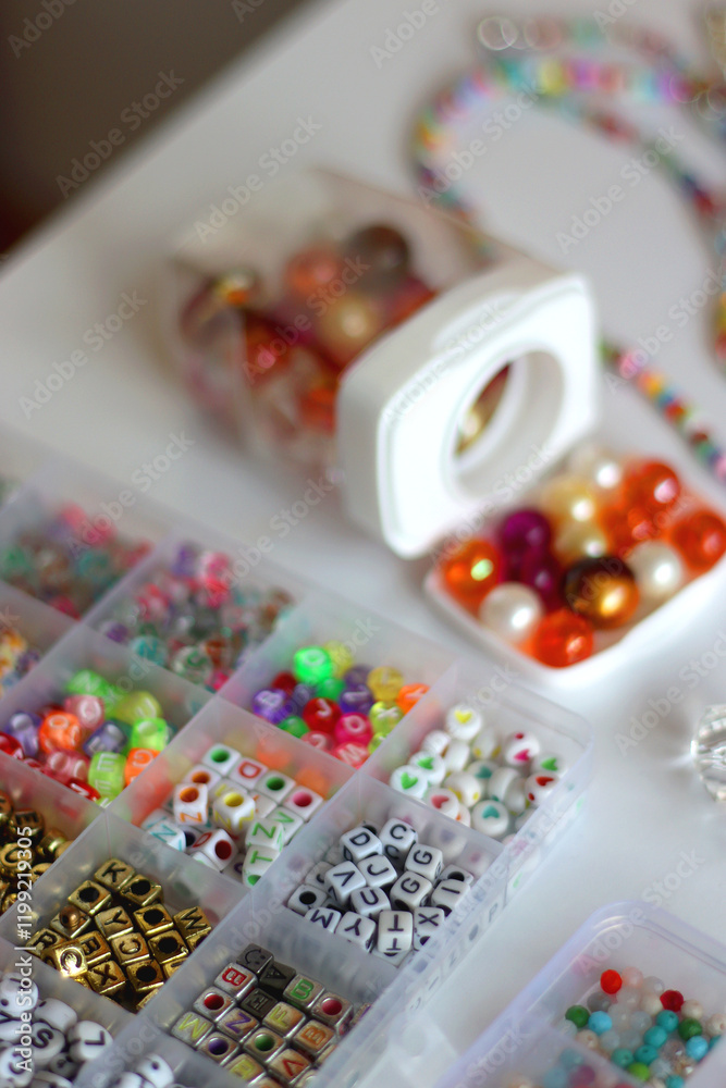 Hand figurine, colorful friendship bracelets, necklaces, various beads and DIY supplies on the table. Making jewelry at home. Selective focus.