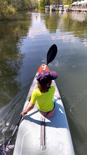 A child paddling a paddleboard on a calm river with family in the background, enjoying peaceful outdoor exploration