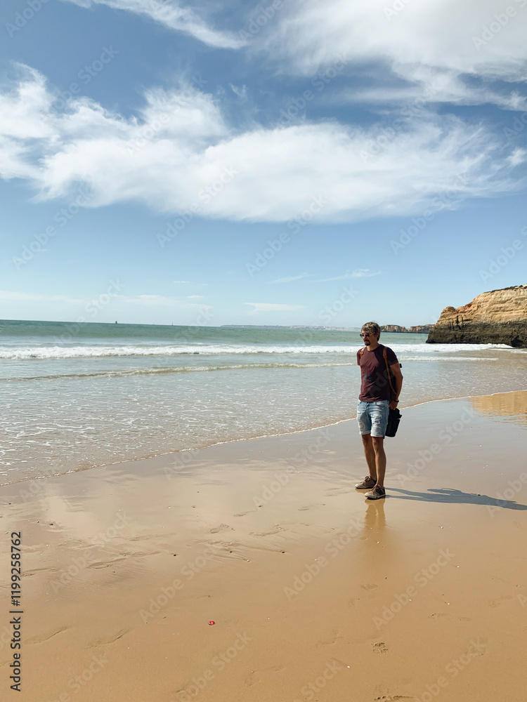Man standing on wet sandy beach in Algarve with ocean waves in background Man standing on wet sandy beach in Algarve with ocean waves in background