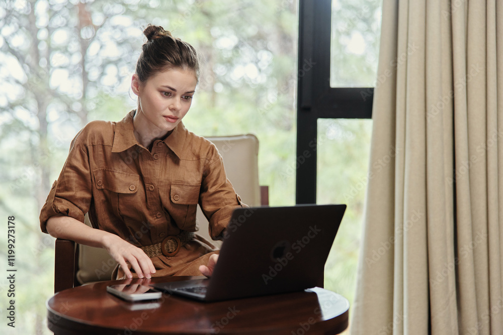Fototapeta premium Young woman working on a laptop in a cozy, modern living space, showcasing a sense of focus and professionalism