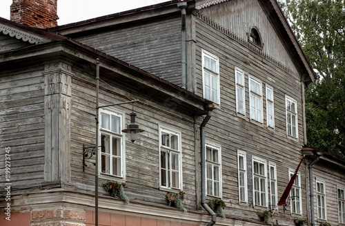 Old wooden house exterior close-up shot with white wooden windows and an old street lantern in the foreground.