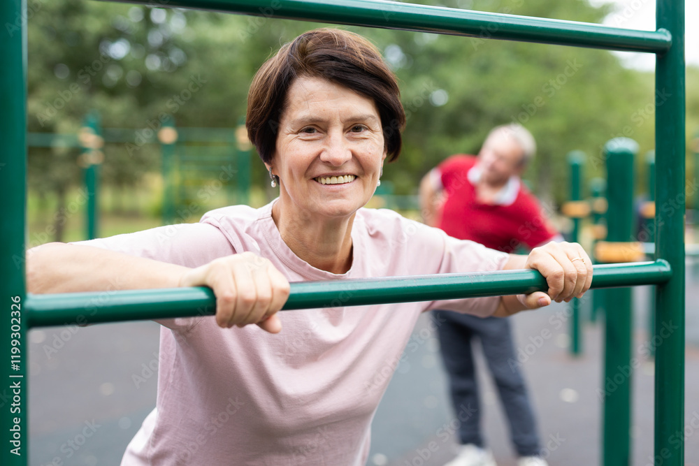 Obraz premium Mature woman doing push-ups from the crossbar on outdoor sports ground