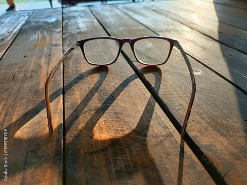 Close up of eyeglasses placed on wooden surface with sunlight reflection.
