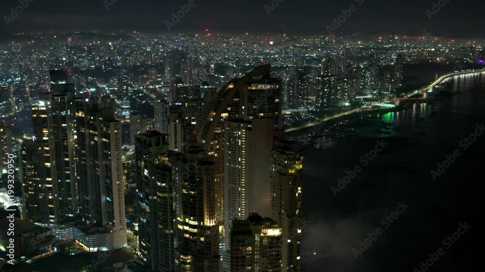 Drone shot of city at night, fireworks in the background lights everything up Drone shot of city at night, fireworks in the background lights everything up