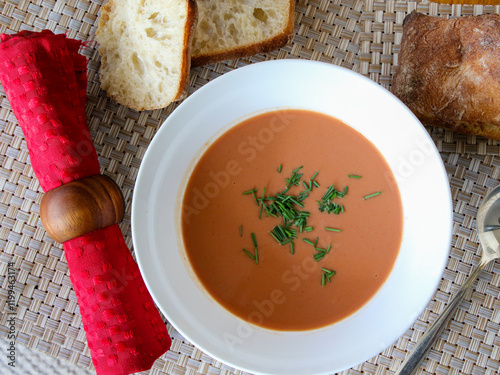Cold tomato soup in a white bowl with bread rolls.