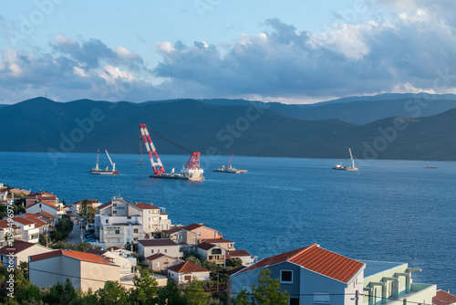 View of residential village Komarna with Peljesac Bridge construction site, cranes, and ships in the Adriatic Sea photo