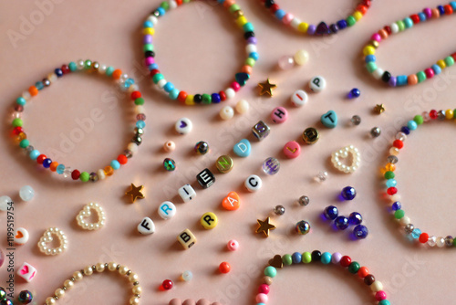 Friendship bracelet spelled with letter beads. Colorful handmade bracelets and various beads. Selective focus, pink background.
