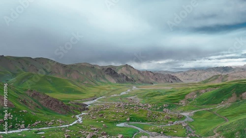 In a fabulous valley, green grass covers the ground, and a mountain road meanders between majestic mountains,passing through deep canyon.The summer sky is blue, emphasizing the beauty of the mountains