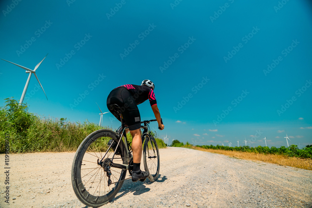 Obraz premium Cyclist enjoying a sunny ride on a gravel road with wind turbines in the background