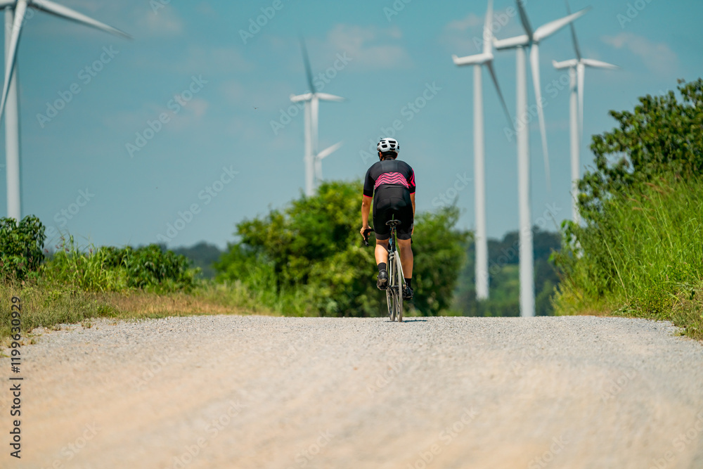Obraz premium Cyclist navigating a gravel road surrounded by wind turbines under a blue sky on a sunny day