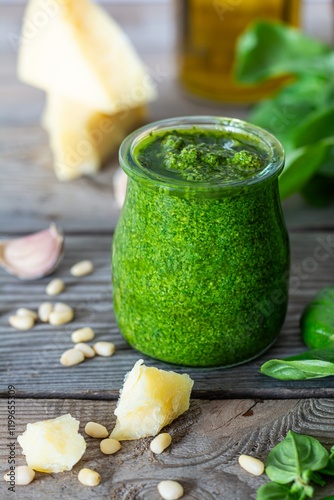 Green pesto in a glass jar made from fresh basil leaves, pine nuts, parmesan, garlic and olive olia on a wooden background. Popular Italian dressing for salads, pasta and pizza.