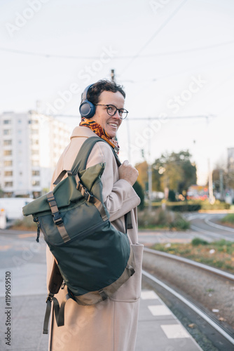 Businesswoman wearing headphones and carrying backpack waiting for her train to go to work