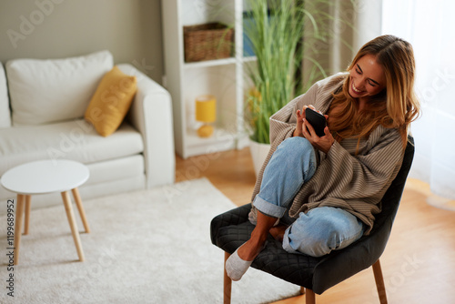 Smiling woman using mobile phone at home while relaxing on armchair