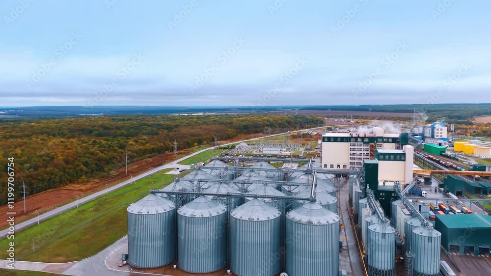 Rising above the silo tanks grouped at the territory of the modern agricultural plant. Loaded trucks and wagons on the railways are at backdrop. Rising above the silo tanks grouped at the territory of the modern agricultural plant. Loaded trucks and wagons on the railways are at backdrop.