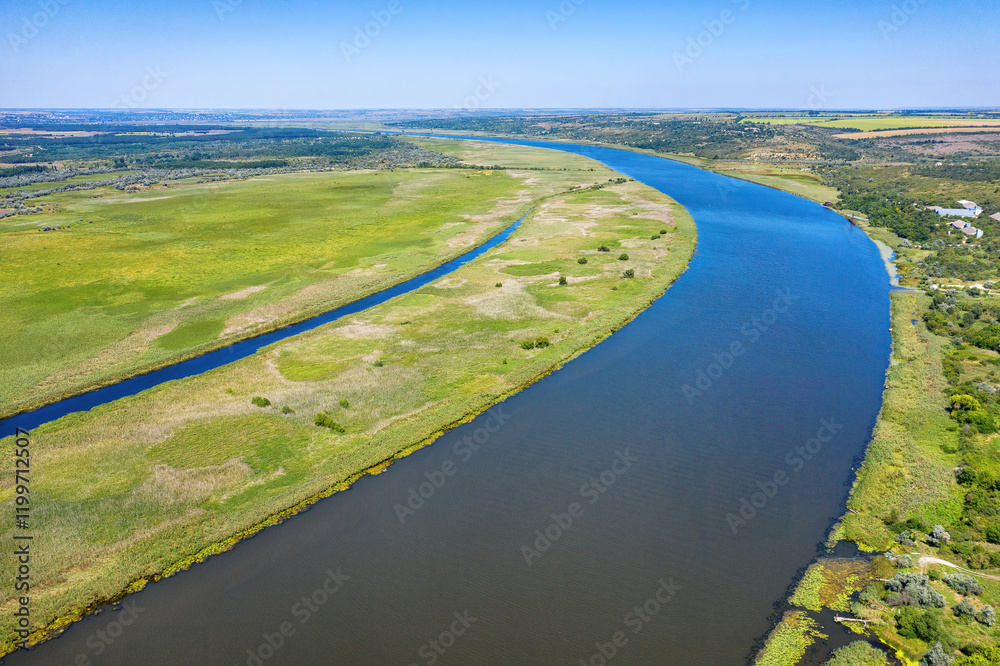 The majestic Southern Bug River winds through lush green landscapes under a clear blue sky during the day. Aerial photo.