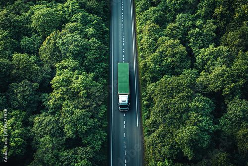Aerial top view of a truck driving on a highway road between a green forest. Sustainable transport with a drone view capture of a truck driving on asphalt road
