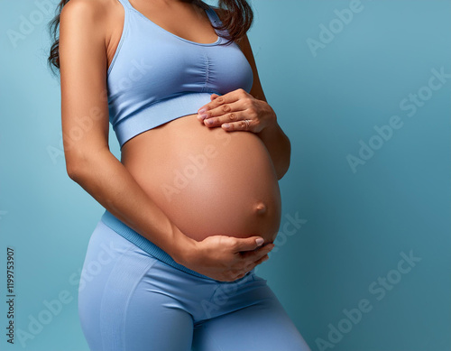 Plano medio de una mujer embarazada con las manos sobre la barriga con ropa deportiva y fondo azul photo