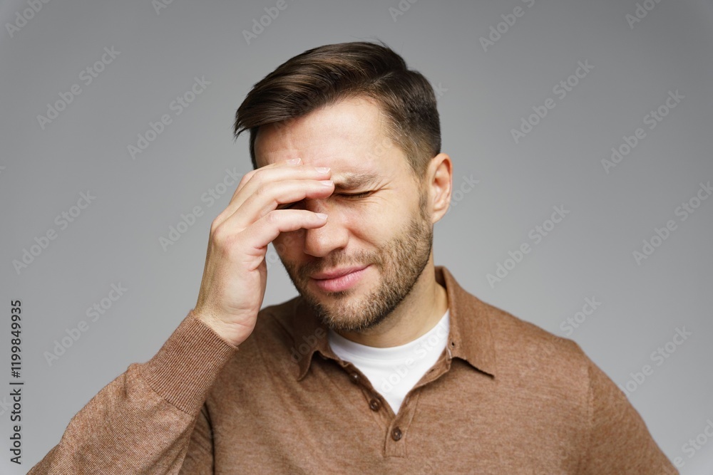 Young man expresses frustration with hand on forehead in a neutral-toned setting Young man expresses frustration with hand on forehead in a neutral-toned setting