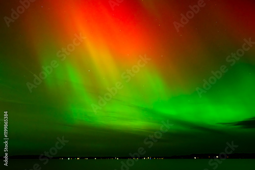 Vibrant red and green auroras (Northern Lights) paint the night sky, creating a mesmerizing and surreal atmosphere over Grand Traverse Bay, Michigan, USA.