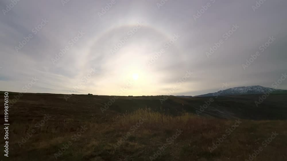 Halo sun effect in wild rocky mountain valley. Yellow field meadow covering grass. Bright sunlight behind clouds. Wonderful natural landscape of national park Halo sun effect in wild rocky mountain valley. Yellow field meadow covering grass. Bright sunlight behind clouds. Wonderful natural landscape of national park