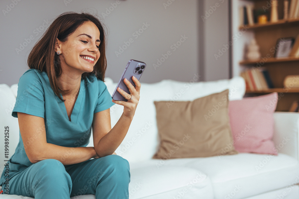 Smiling Woman in Scrubs Using Smartphone in Cozy Living Room Smiling Woman in Scrubs Using Smartphone in Cozy Living Room