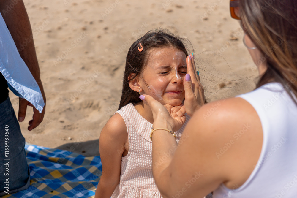 Fototapeta premium Mom carefully applying sunscreen to her daughter's face during a sunny day at the beach