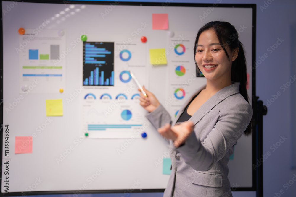 Businesswoman pointing at charts and graphs on whiteboard during a presentation, explaining company strategy and financial results to colleagues in meeting room Businesswoman pointing at charts and graphs on whiteboard during a presentation, explaining company strategy and financial results to colleagues in meeting room