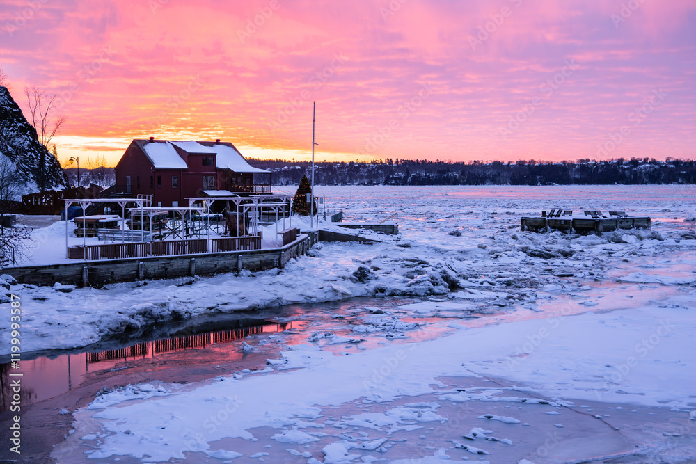 Fototapeta premium Winter sunrise view of the Cap Rouge river flowing into the St. Lawrence River partly covered in ice, with the marina installations on the shore, Quebec City, Quebec, Canada