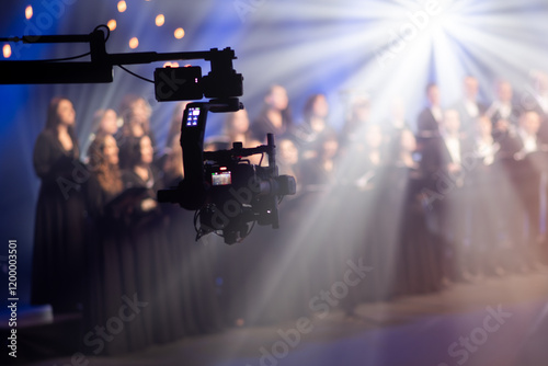 Close-up of a camera crane filming a choir performance with dramatic lighting in a studio