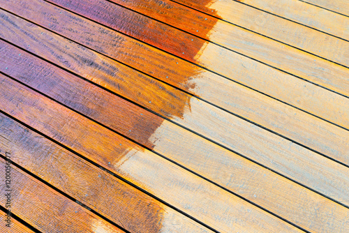Close-up of a wooden deck showing the process of restoration with a half-stained surface contrasting weathered and treated wood during a home improvement project. photo