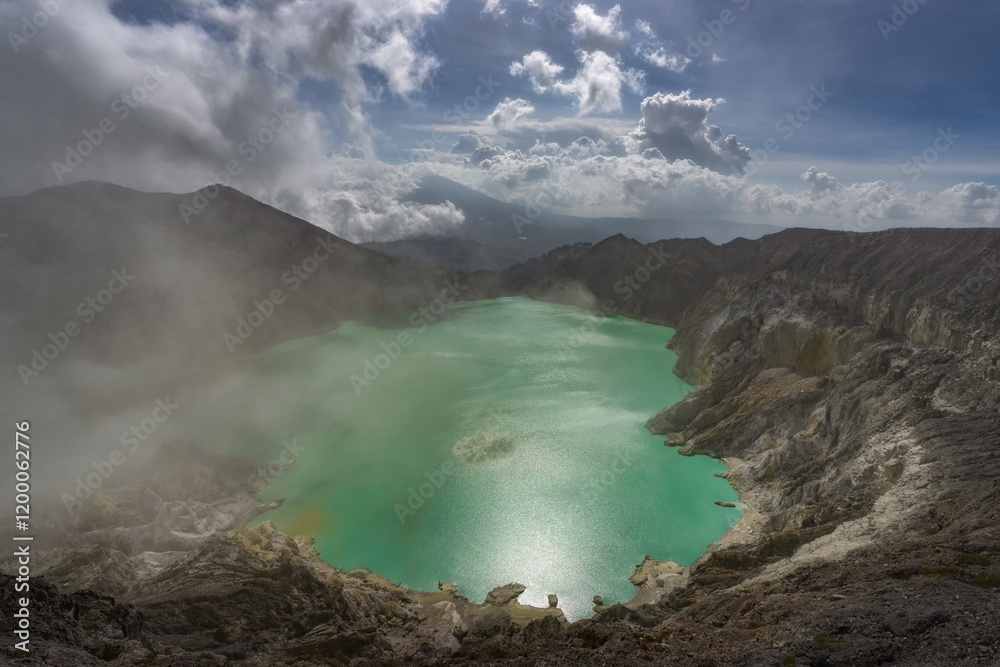 The breathtaking view of a vibrant turquoise crater acid lake, beautifully nestled in rugged mountainous terrain, is enveloped in a gentle mist and soft clouds, East Java, Ijen Volcano, Indonesia