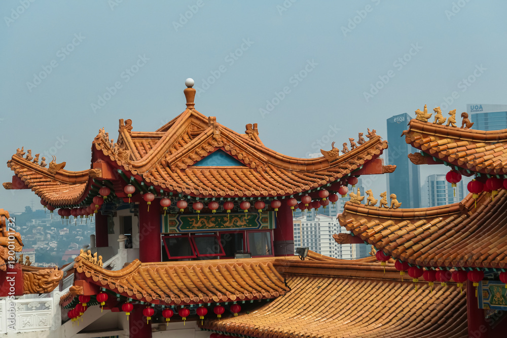 Fototapeta premium Iconic architecture of Chinese Thean Hou Temple. Roof is adorned with vibrant colors, intricate patterns, decorative figures. Rows of red lanterns. Cityscape of Kuala Lumpur, Malaysia, Southeast Asia