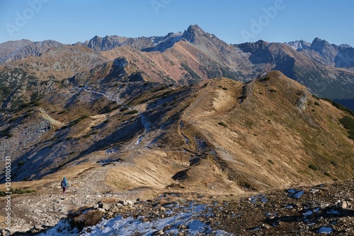 Panorama of Czerwone Wierchy range from around Kasprowy Wierch Peak, Tatras Mountains, Poland. During trekking red trail on sunny autumn day. Little silhouettes of people on trail.