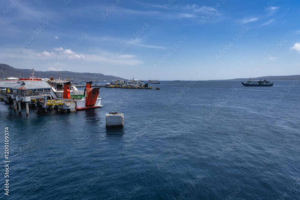 A picturesque harbor scene that showcases an array of ferry boats used for Java Bali crossing, peacefully resting on calm waters beneath a beautiful blue sky, East Java, Indonesia