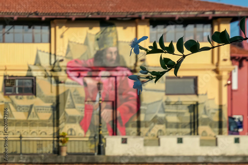 Building in Melaka, Malaysia, features large mural of historical figure (Portuguese or Dutch) due to Melaka's colonial past. Mural is painted on a yellow wall against backdrop of residential buildings